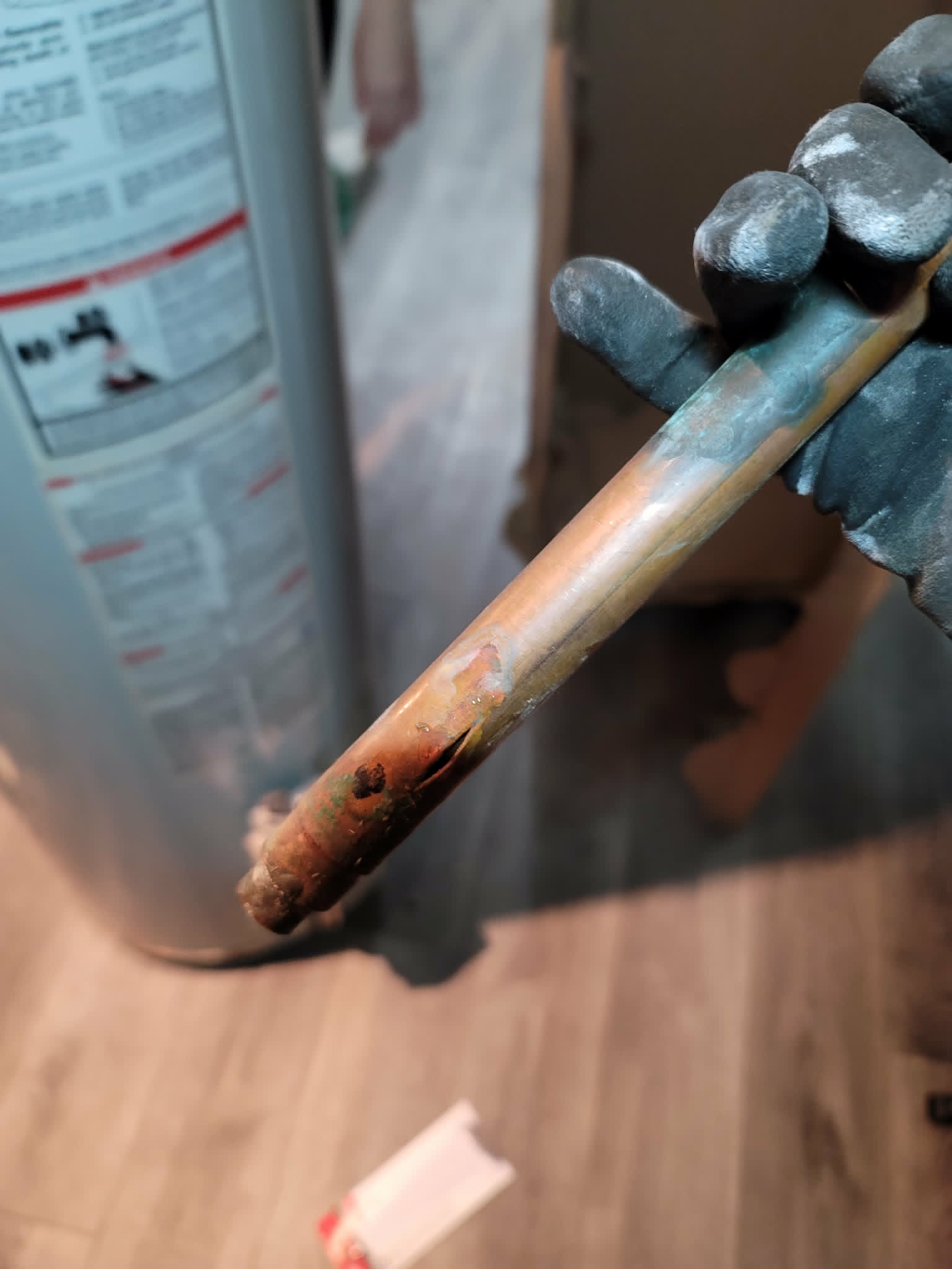 A copper water pipe split open lengthwise from freezing, held in a gloved hand